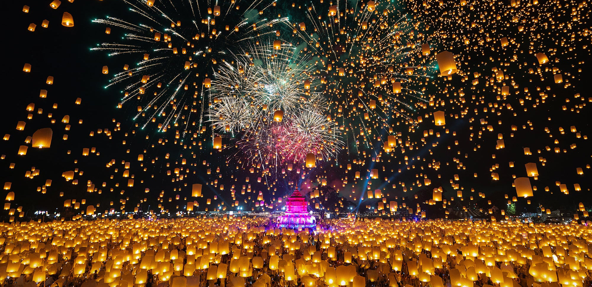 Massive display of floating lanterns and fireworks at night, likely during Yi Peng festival, supported by Travel X.